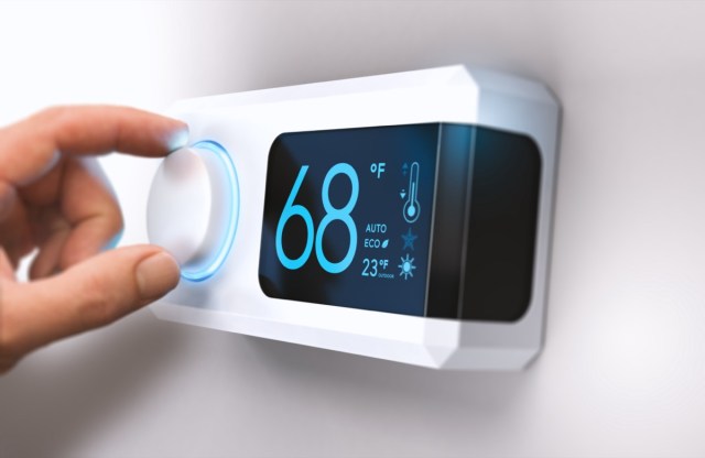 hand turning a home thermostat knob to set temperature on energy saving mode