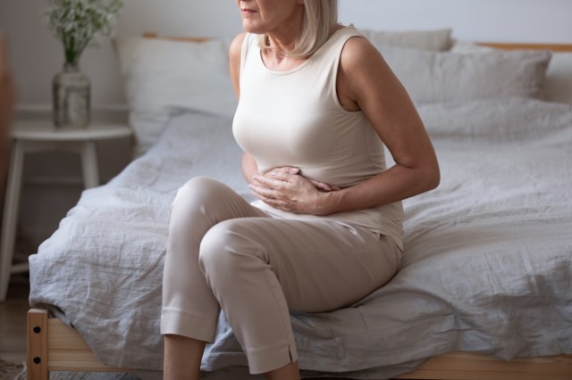 middle aged woman sitting on bed with stomach pain