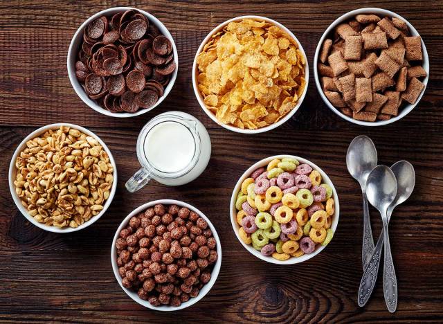 six bowls of different kids' cereals with spoons and glass of milk