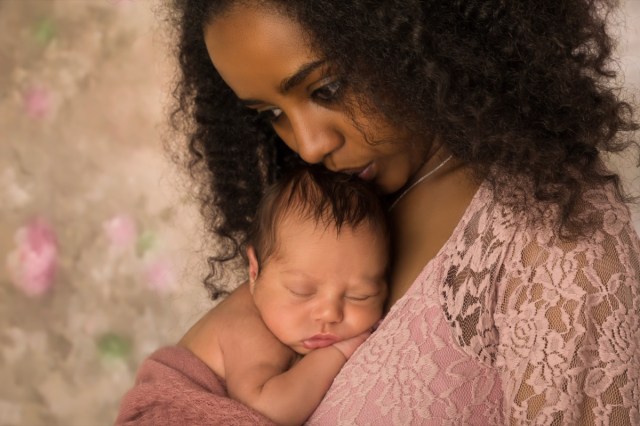 mother in pink lace dress holding her 1 week old little baby