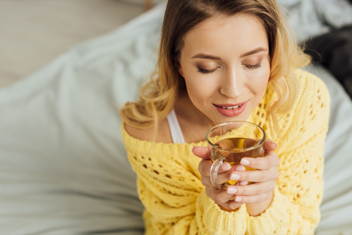 woman with eyes closed holding cup of tea at home