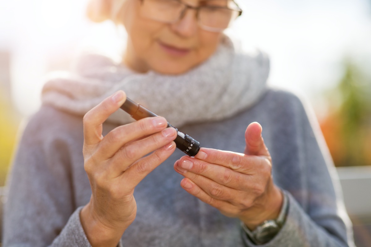 woman checking blood sugar level while sitting on bench