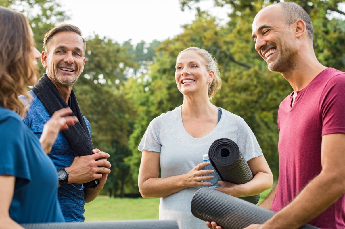 group of mature people holding yoga mat and towel in conversation after exercising at park