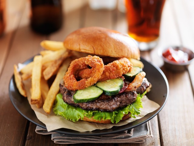 large cheeseburger loaded with onion rings, bacon and bbq sauce served with french fries