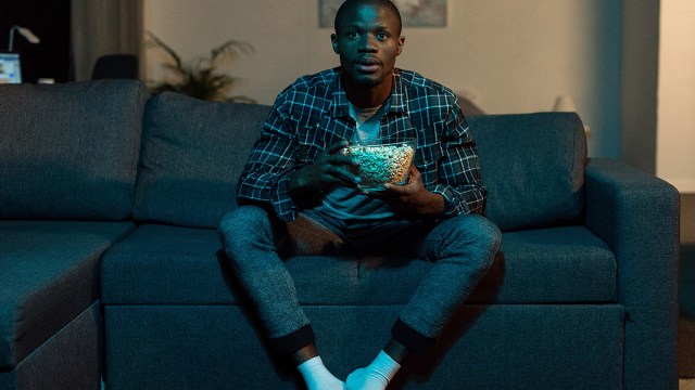 man watching tv on couch holding popcorn bowl