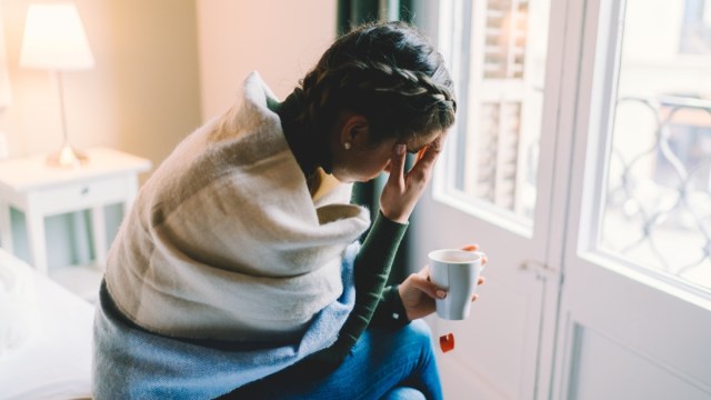 woman with temperature staying home wrapped in scarf and drinking hot tea.