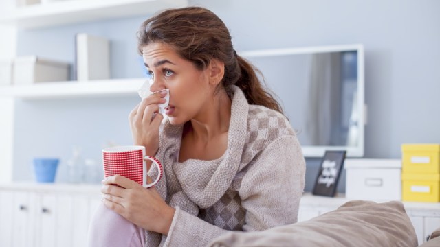 sick woman blowing nose on her sofa.