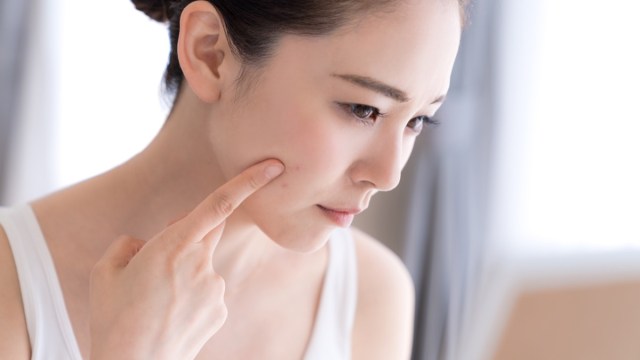 young woman looking in mirror touching face