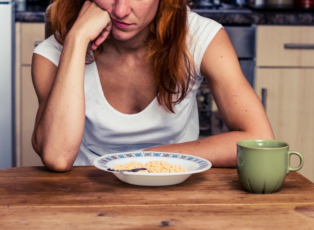 woman looking bored staring at bowl of cereal