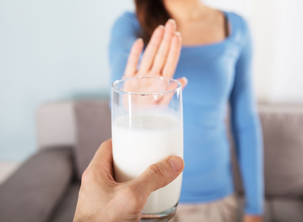 woman holding up an outstretched hand saying no to a man offering her a glass of dairy milk