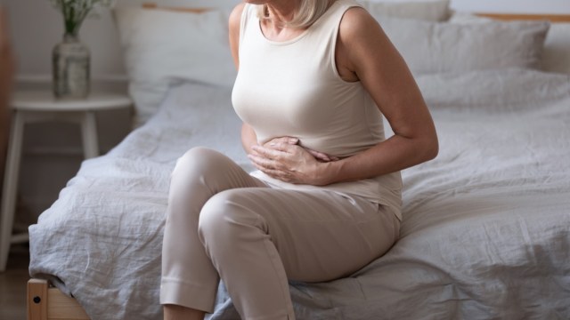 middle aged woman sitting on bed with stomach pain