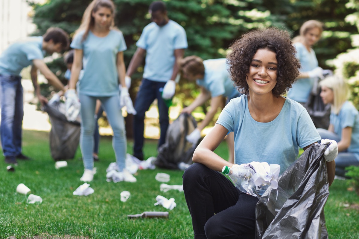 happy woman and group of volunteers with garbage bags cleaning area in park copy space