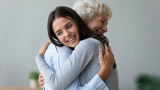 happy young adult daughter granddaughter visiting embracing hugs old retired grandmother hugging