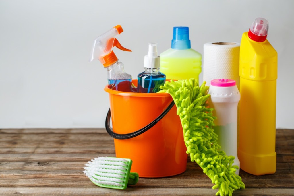 bucket with cleaning items on light background