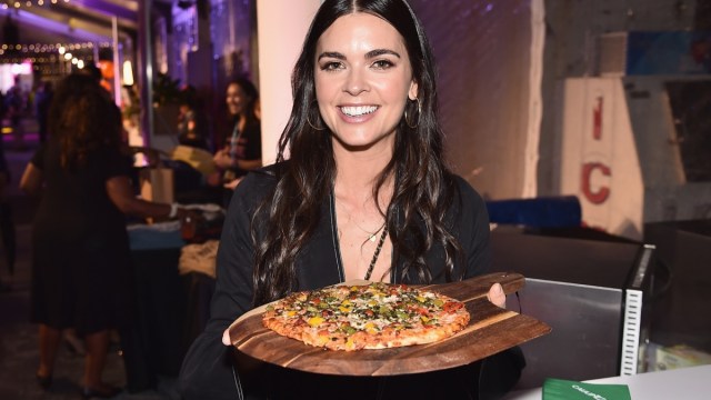 katie lee biegel holds a pan with pizza on it