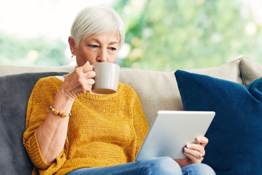 senior woman using a digital tablet and having coffee on the sofa at home.