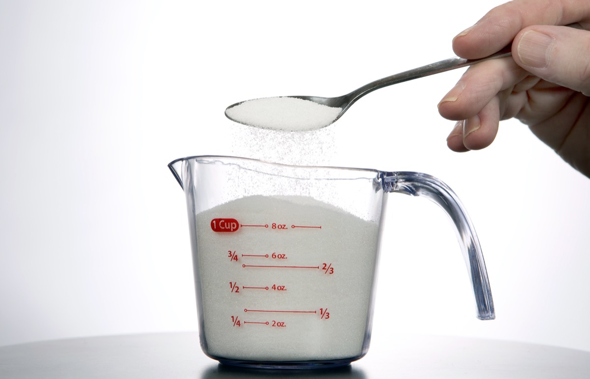 the man pours a spoonful of sugar into a measuring cup.