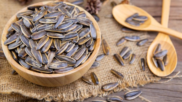 wooden bowl of sunflower seeds on piece of burlap next to two wooden spoons