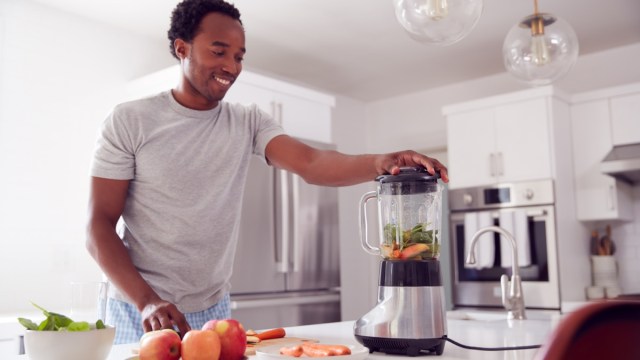 young man making smoothie in modern kitchen