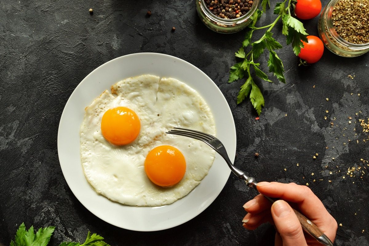 person eating two eggs from a white plate