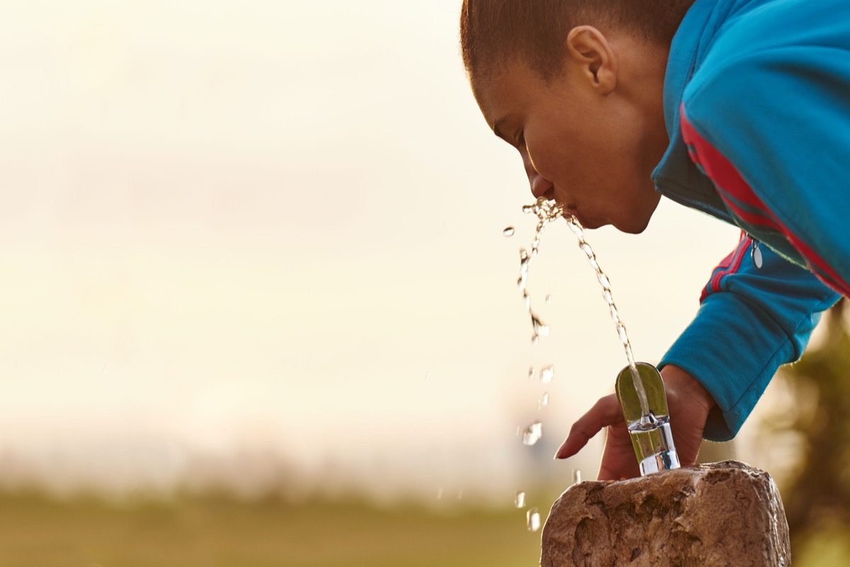 close-up of a young mixed girl busy drinking water from a fixed fountain station with beautiful copy space