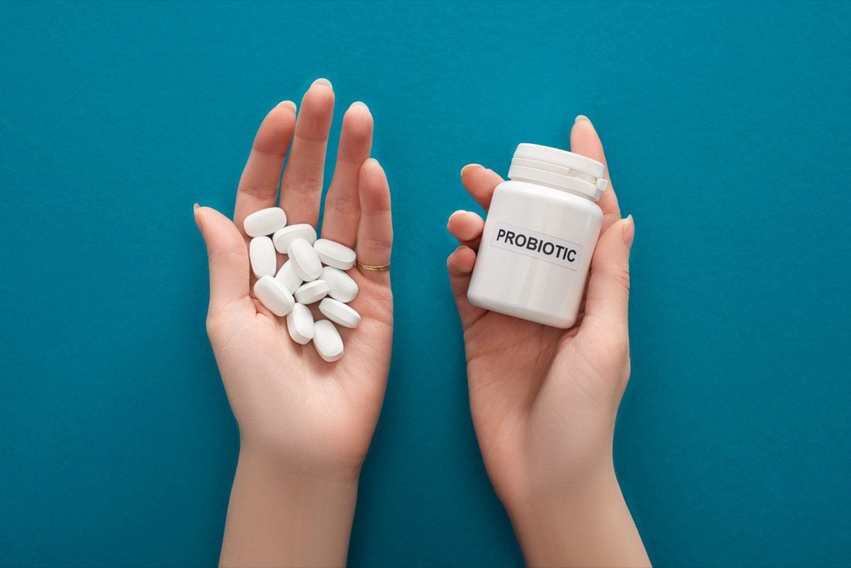 woman holding white probiotic container and pills in her hands.