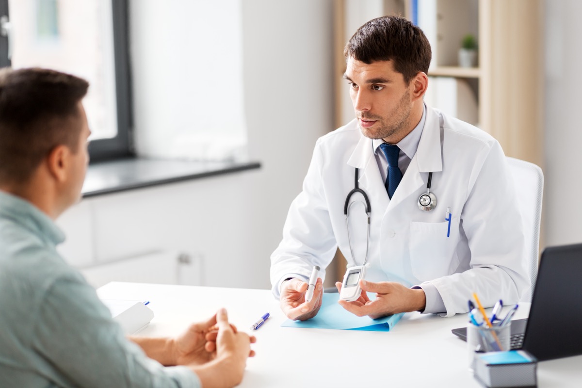 doctor with glucometer and insulin pen talking to male patient at medical office in hospital