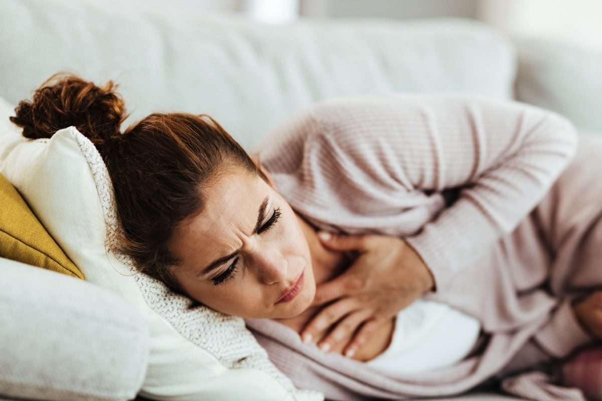 woman having chest pain and coughing while lying on sofa at home.