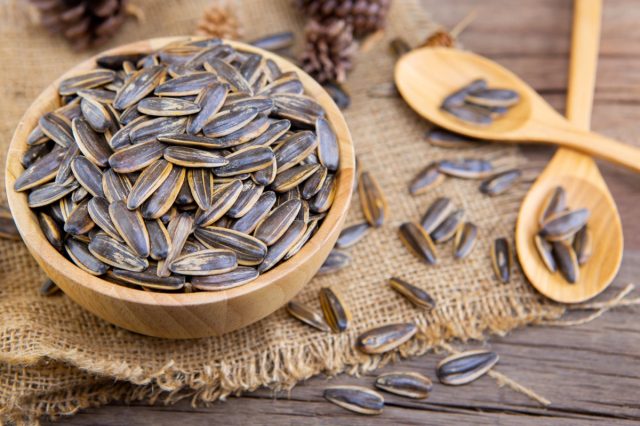 wooden bowl with sunflower seeds on a piece of burlap next to two wooden spoons