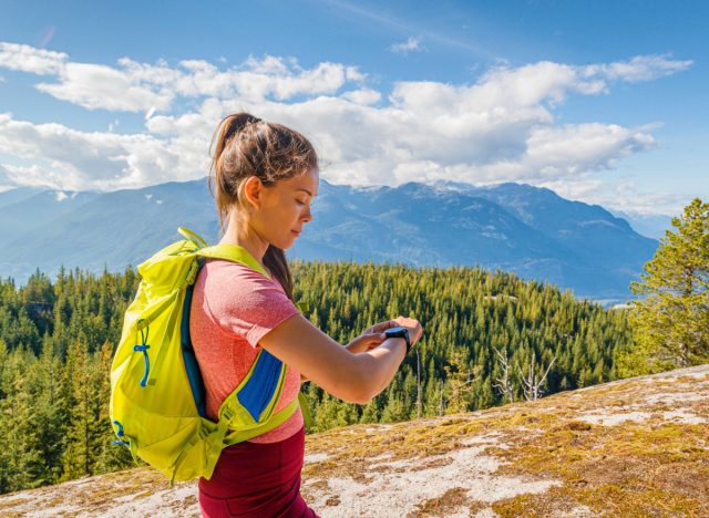 female hiker carrying backpack on top of mountain looking at clock