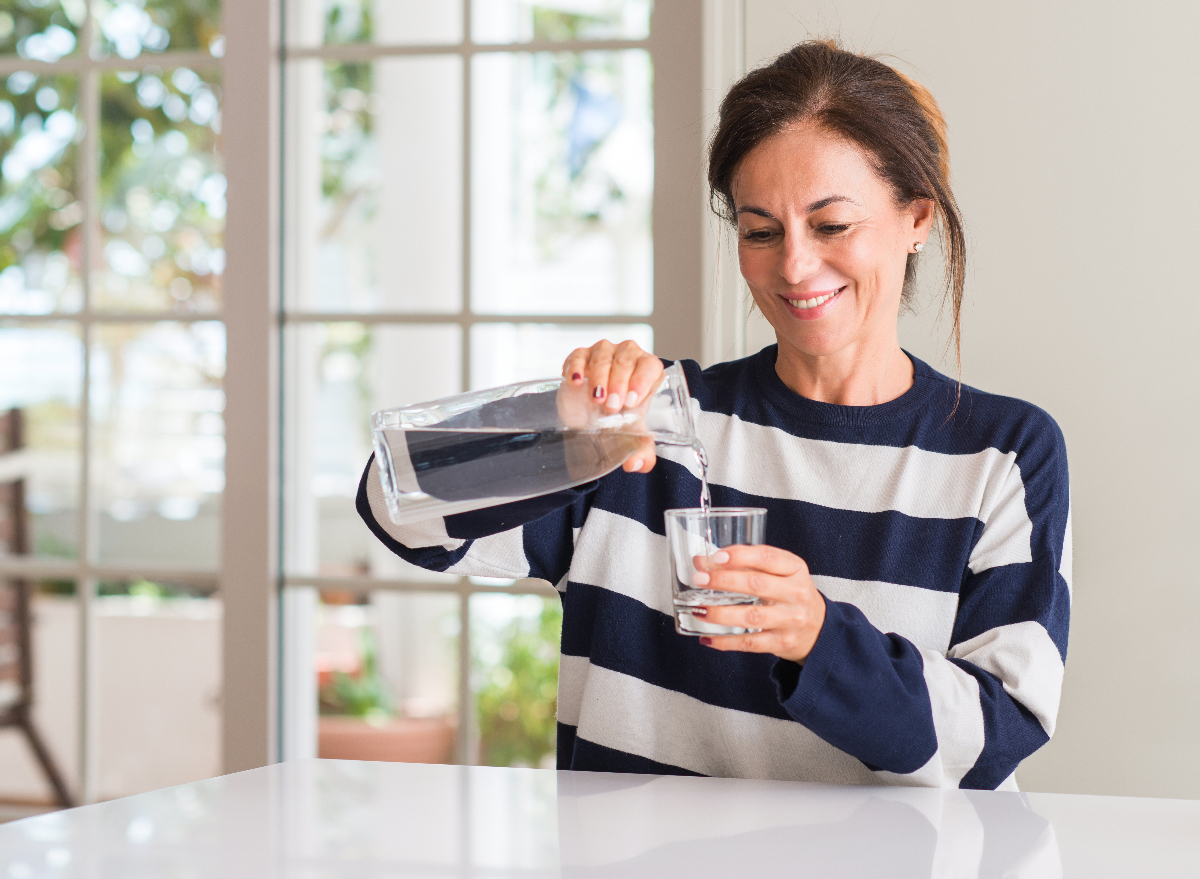 mature woman pours a glass of water in her kitchen