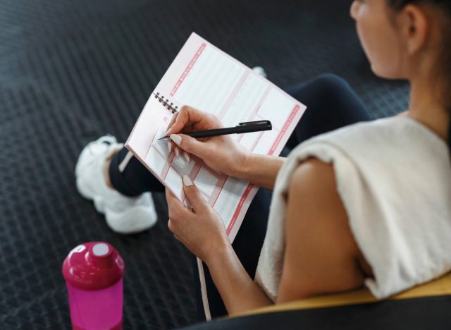 close-up of woman writing in fitness calendar at gym