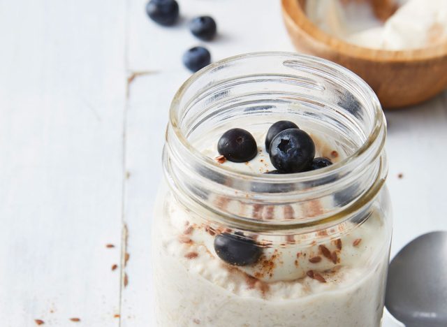 overnight cinnamon rolled oats in open glass jar with blueberries on wooden board with spoon