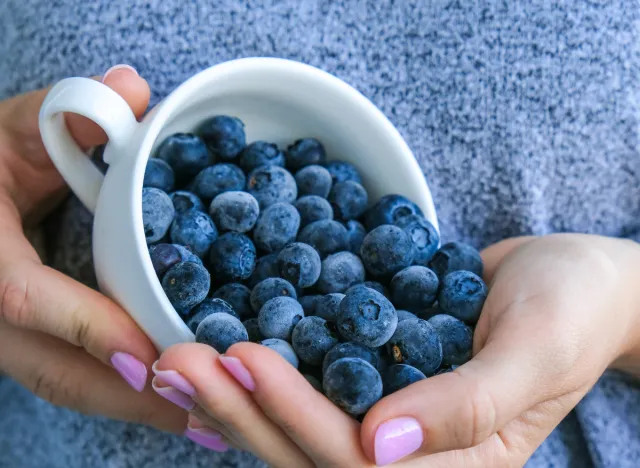 close-up woman pouring cup of blueberries in her hand, food to burn belly fat