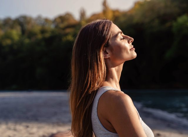 woman with closed eyes basking in the sun while meditating outdoors on a beach