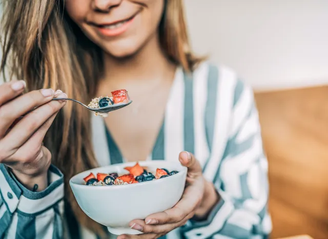 close-up woman holding a bowl of oats and fruit, concept of breakfast habits to curb cravings and lose weight