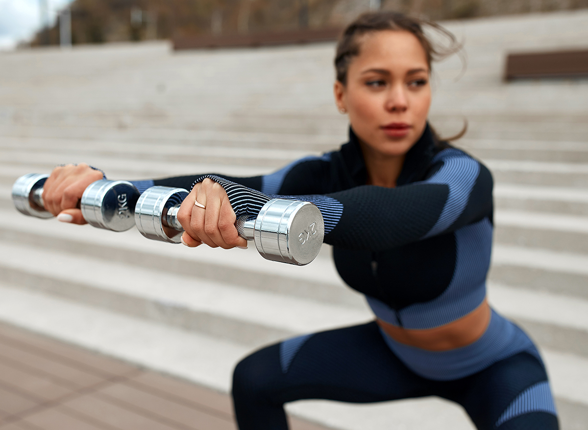 sports girl jumping with dumbbells. photo of a sports girl with a perfect body against the background of the city. strength and motivation. squat with a load