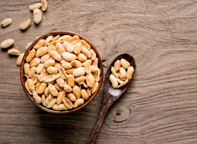 bowl of peanuts with a spoon of peanuts next to it on a wooden table