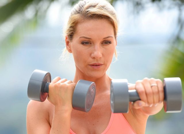 middle aged woman doing dumbbell exercises outdoors, concept of free weight training to regain muscle mass