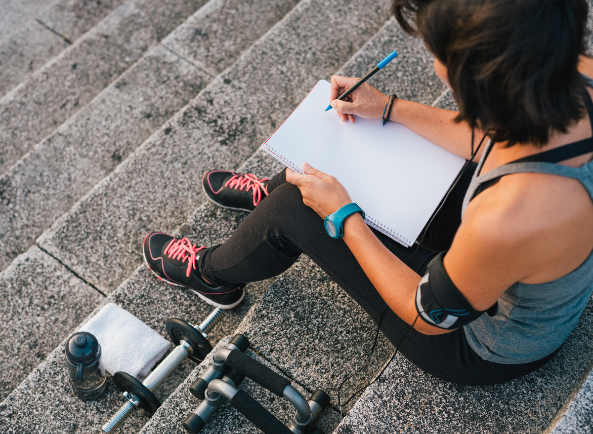 woman keeping track of fitness and weight loss goals in diary, concept of how to lose your big belly by setting goals