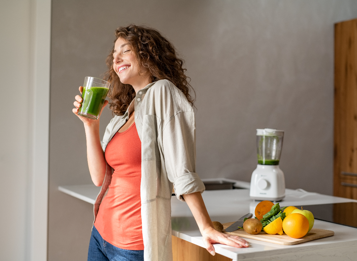 happy woman drinking green juice in the kitchen, concept of tips to lose 20 pounds