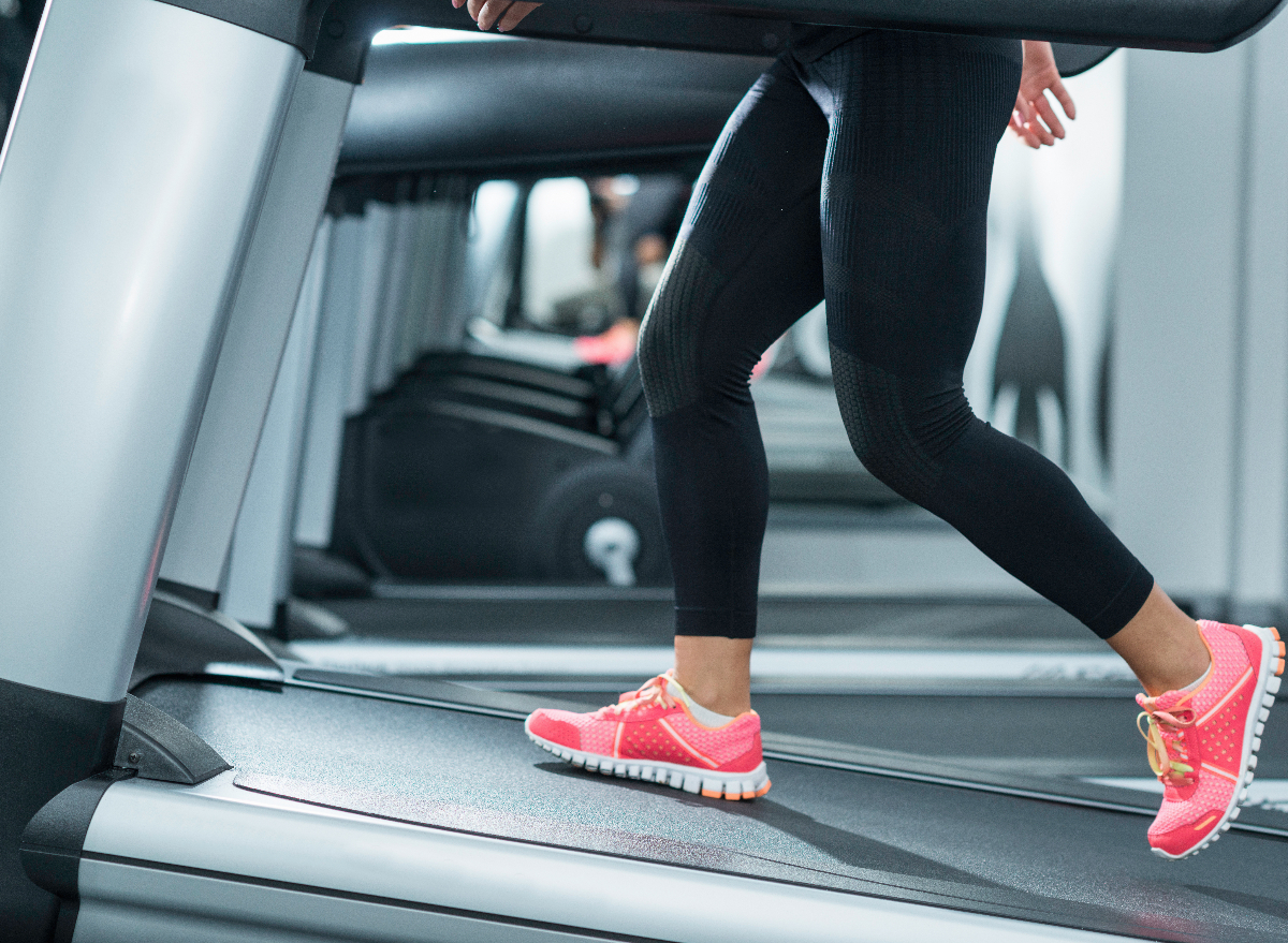 close-up woman walking on treadmill incline to speed up belly fat loss at gym during treadmill workout