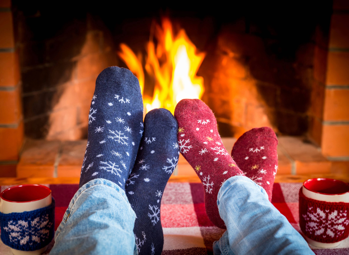 close-up of couple's feet in christmas stockings in front of fireplace next to christmas mugs