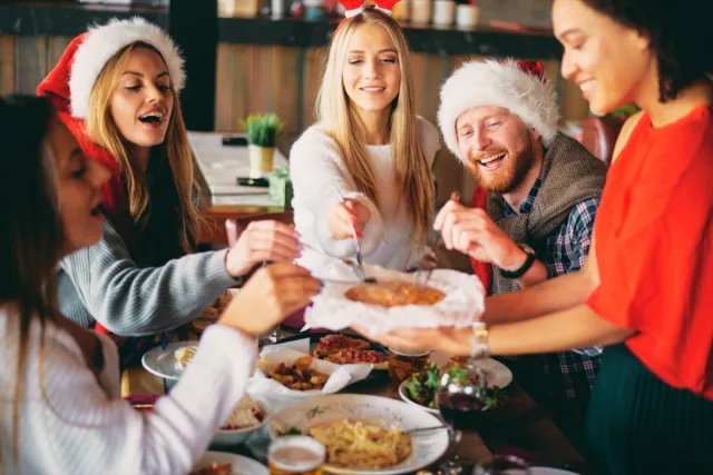 group of 20- or 30-something friends eating a holiday meal together in santa hats