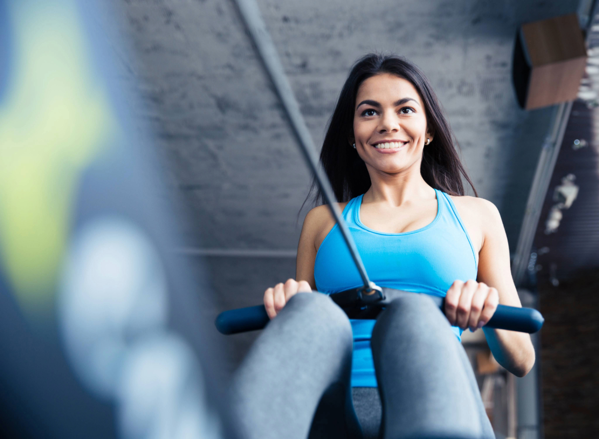 fit happy brunette woman with rowing machine at the gym