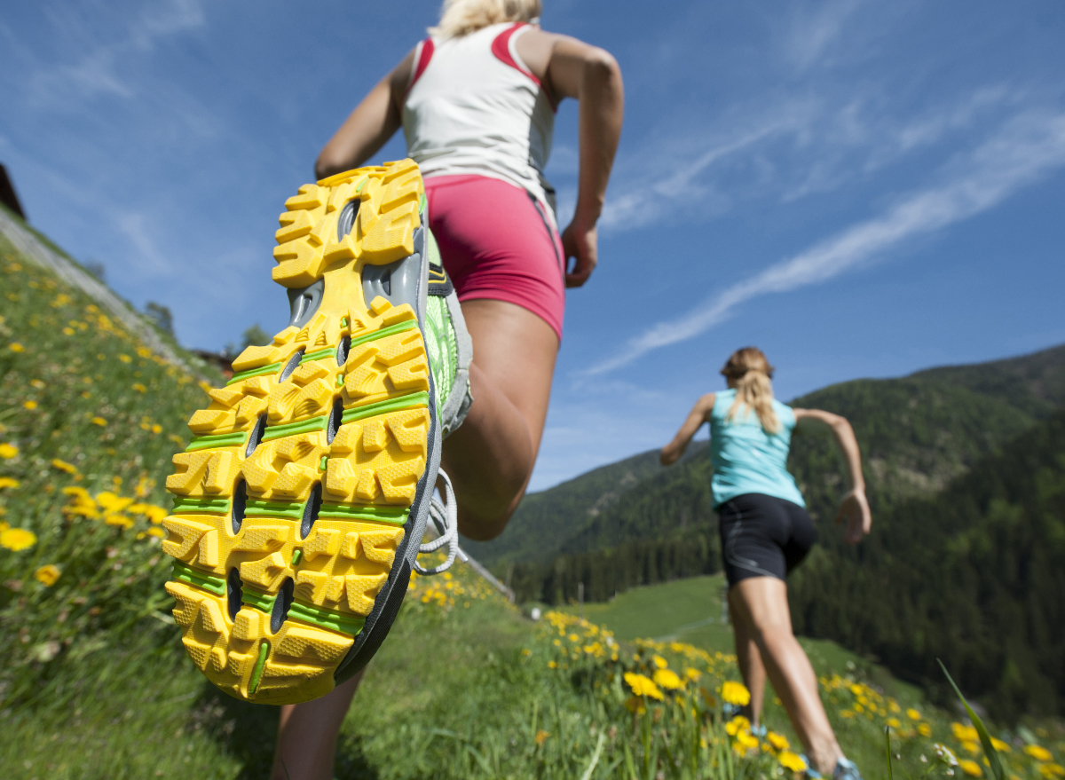 close up bottom of running shoe, two women running through the field, concept of worst running shoes that hurt your feet