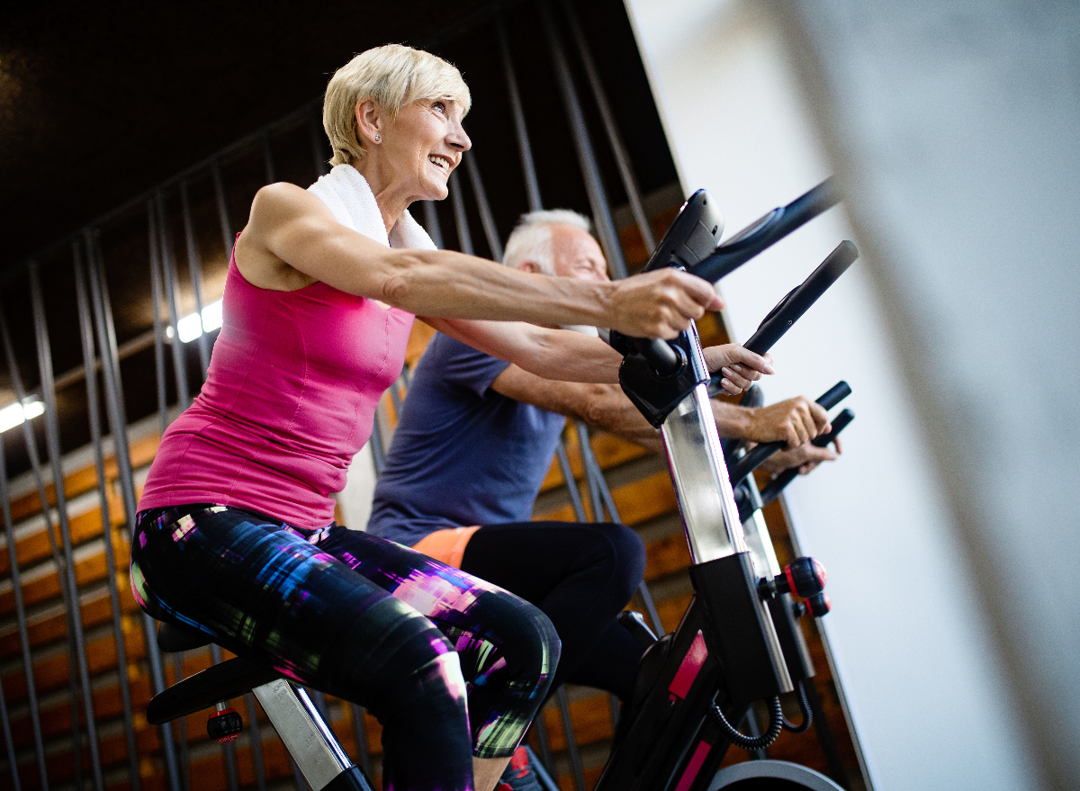 two older adults cycling indoors at the gym