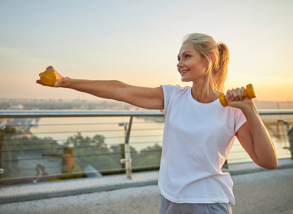 woman outdoors doing arm exercises with dumbbells for skinny arms