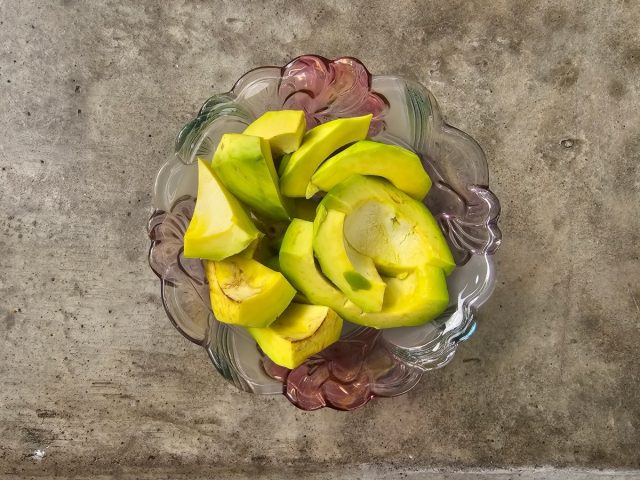 sliced ​​avocado in glass bowl on cement table top view