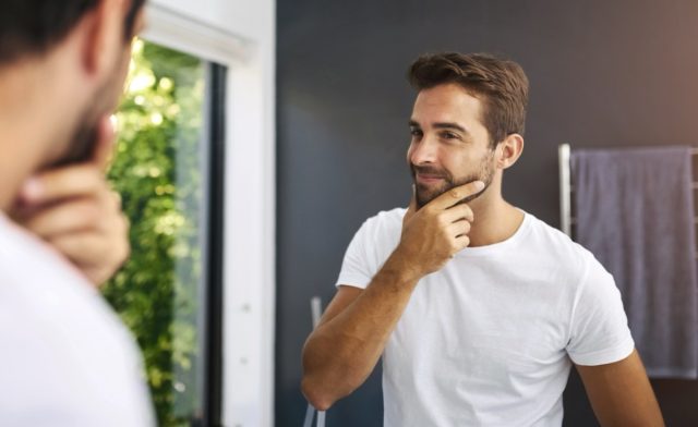 happy man in front of a mirror applying skin care